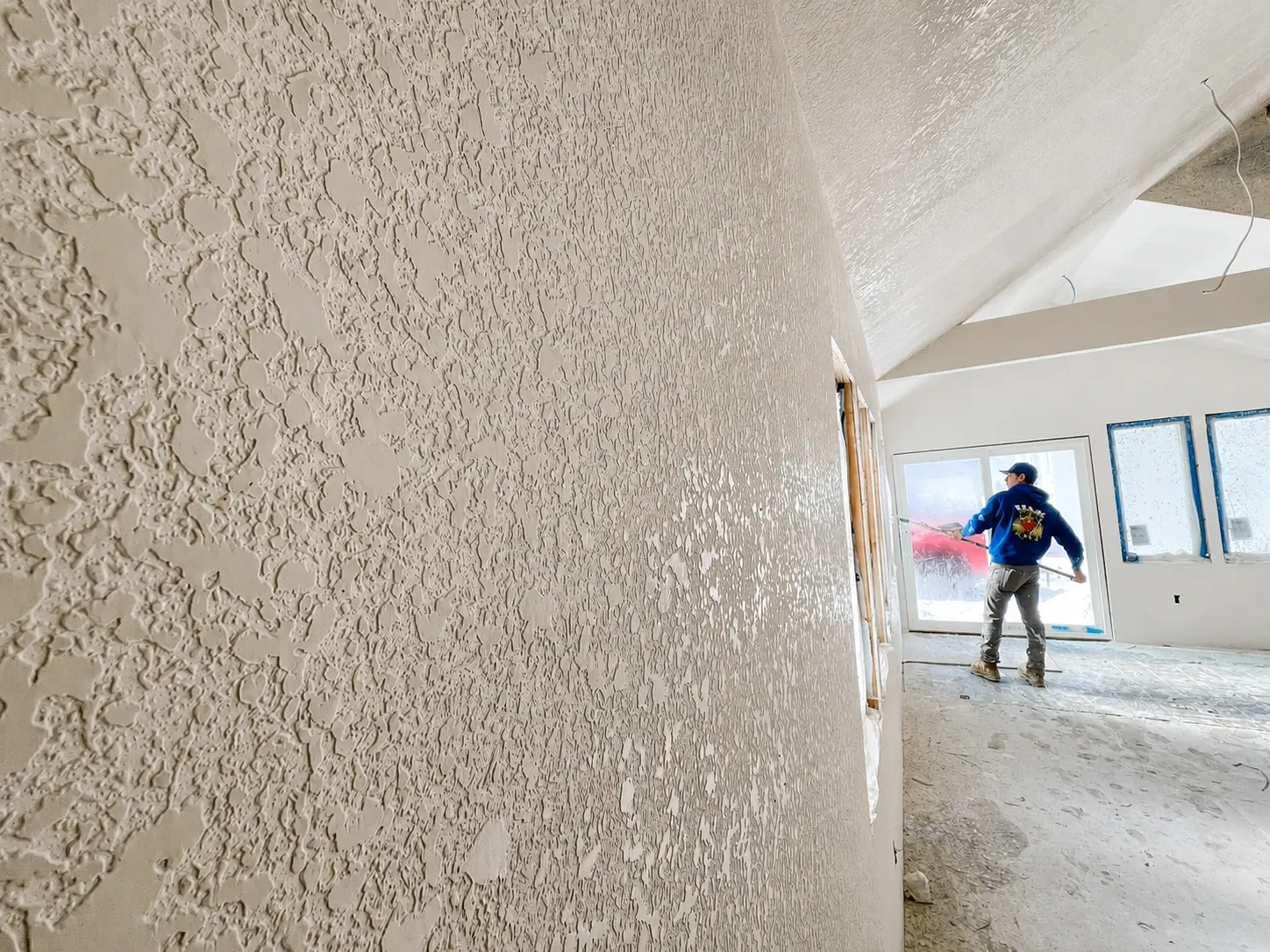 H&K crew member spraying knockdown texture inside a new construction home with vaulted finished ceilings