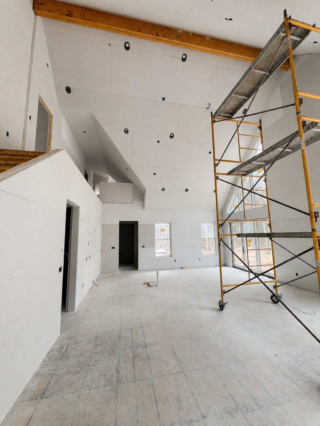 Large builder project — new home under construction with vaulted great room drywall hung and scaffolding in place