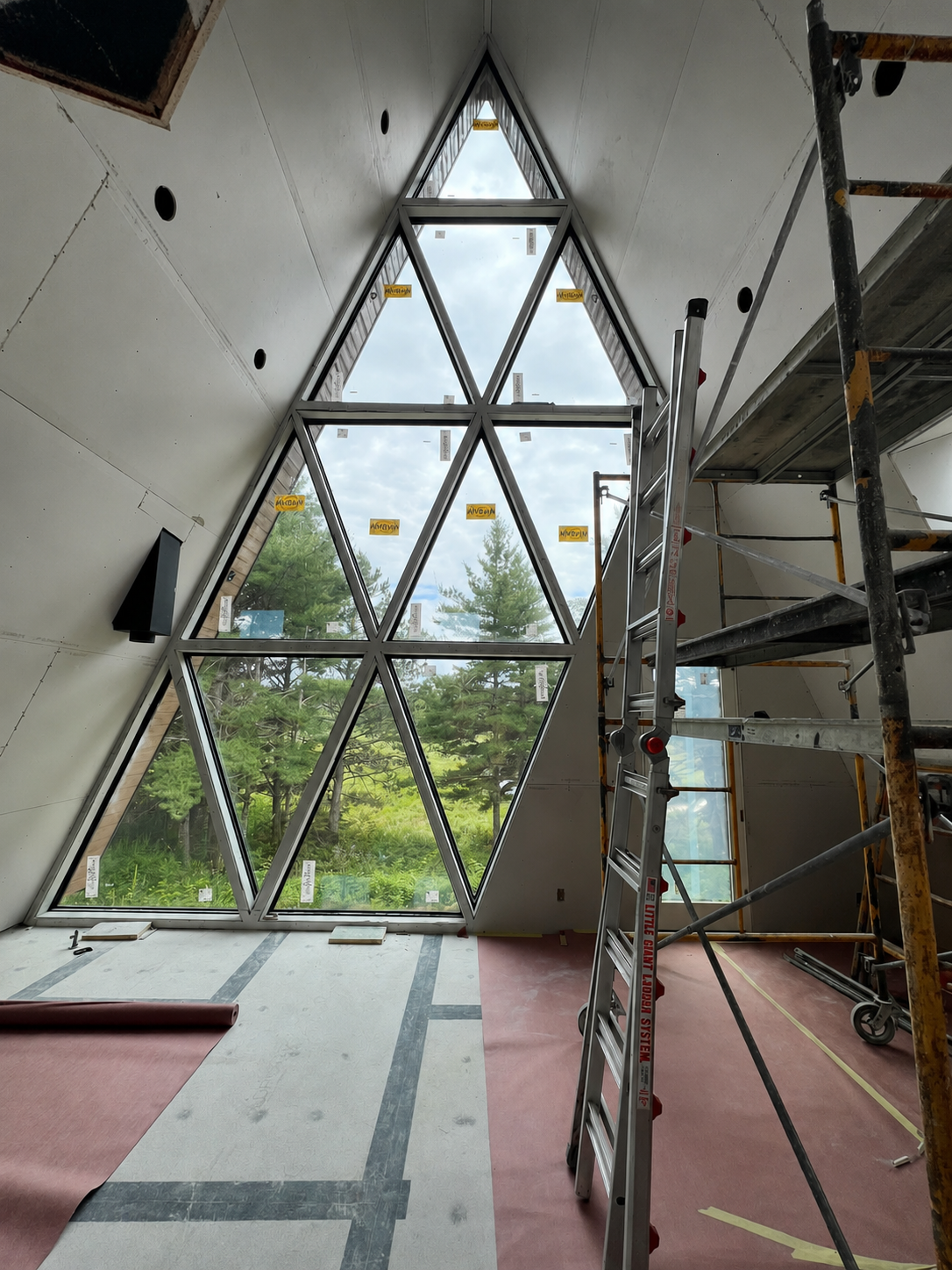 Northwoods build site interior with a tall triangular window wall looking out over pine trees